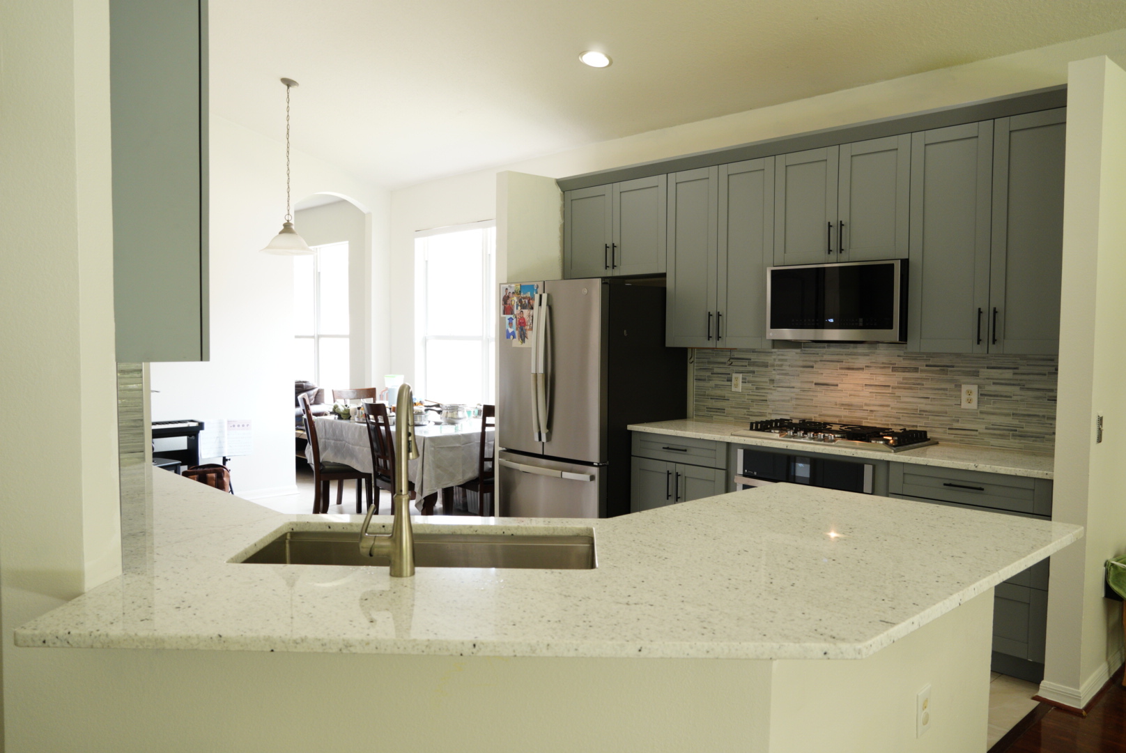 Grey shaker kitchen with white speckled quartz countertops and a glass mosaic backsplash