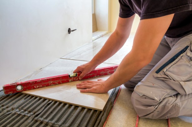 A tiler checking a run of floor tiles with a red spirit level over combed adhesive